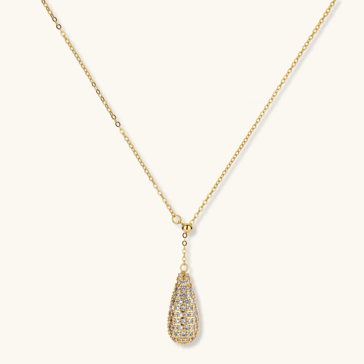 Gold-plated teardrop necklace and earrings covered in AAA cubic zirconia crystals on cream background.
