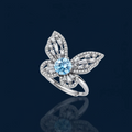Sterling silver ring with blue moissanite center stone surrounded by clear stones in butterfly wing pattern on white background