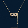 Gold infinity pendant with baguette crystals on adjustable chain against cream background.