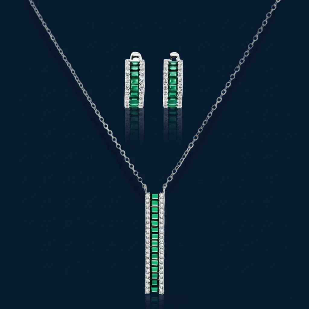 White gold plated jewelry set with emerald green rectangular stones and clear crystals in geometric rows on white background.