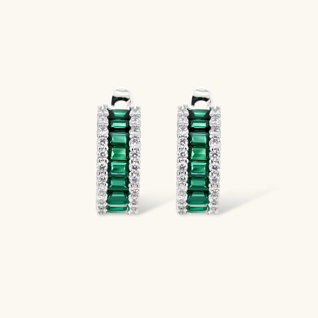 White gold plated jewelry set with emerald green rectangular stones and clear crystals in geometric rows on white background.